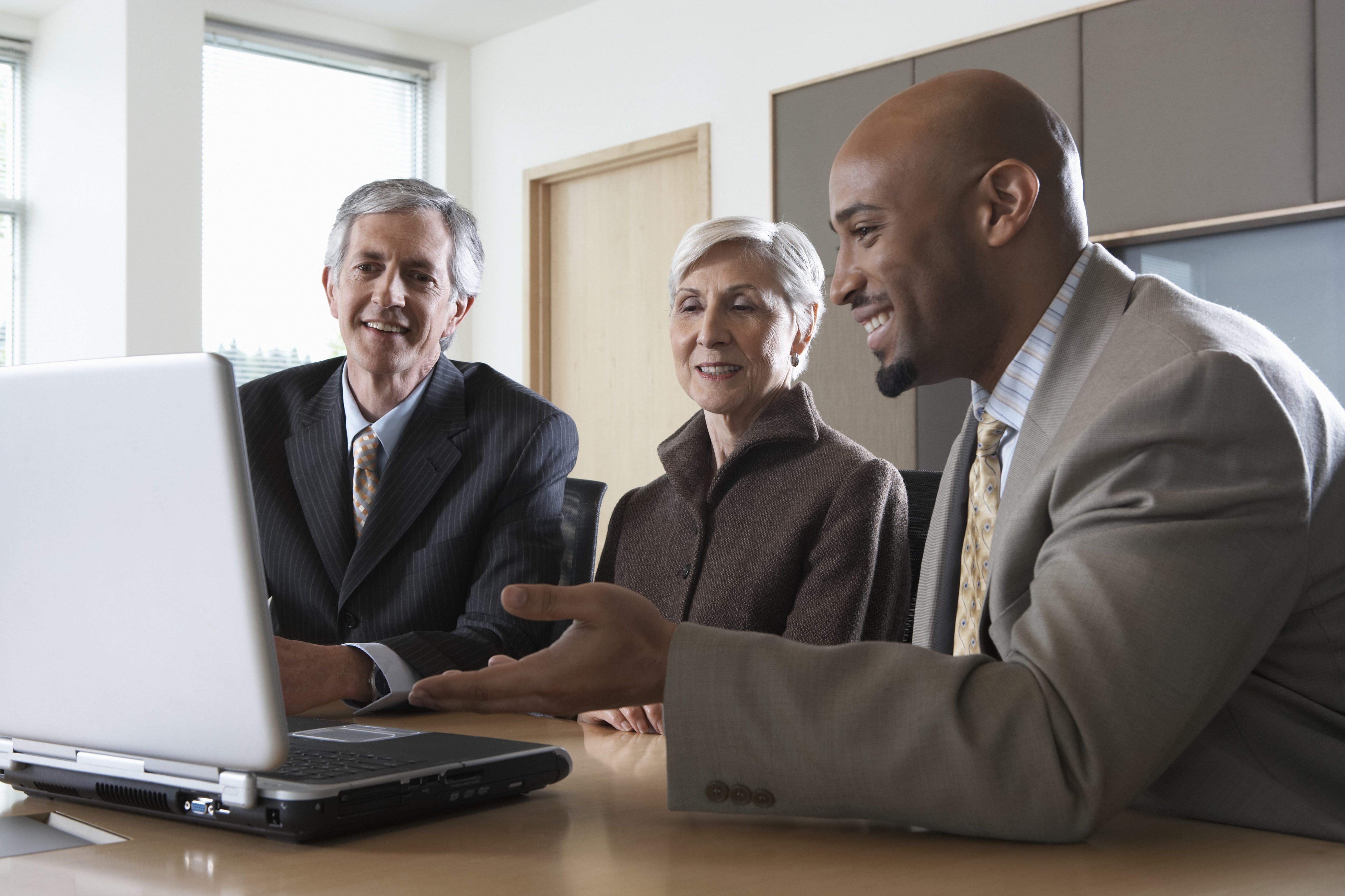 Three executives using laptop during meeting in boardroom, smiling