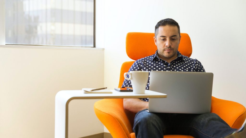 person on their laptop while sitting in an orange chair