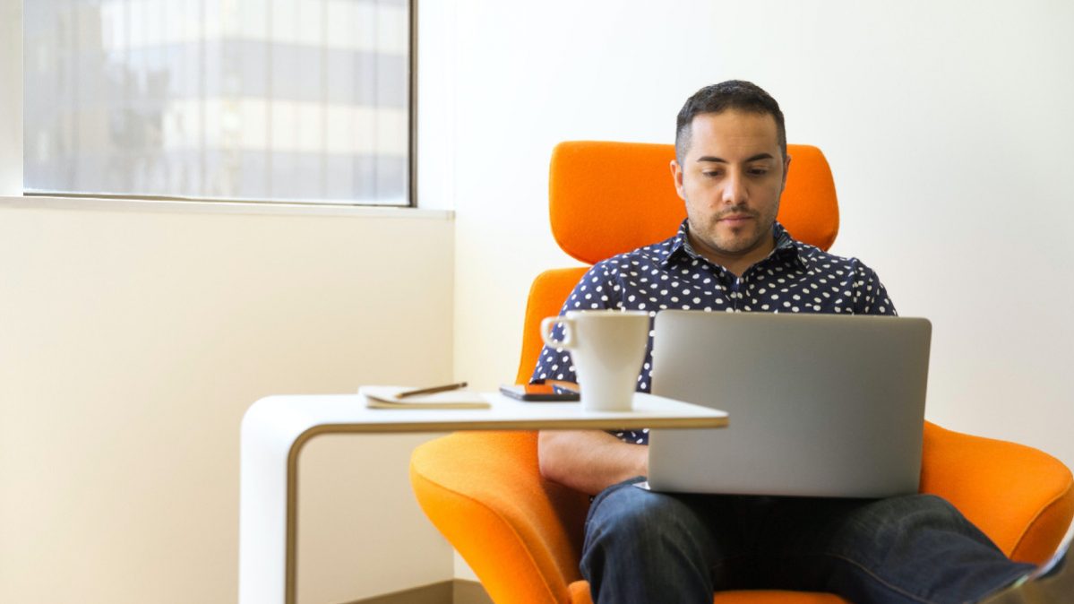 person on their laptop while sitting in an orange chair